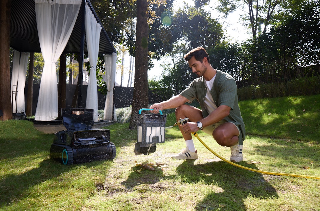 Man watering a robotic lawnmower in a garden.
