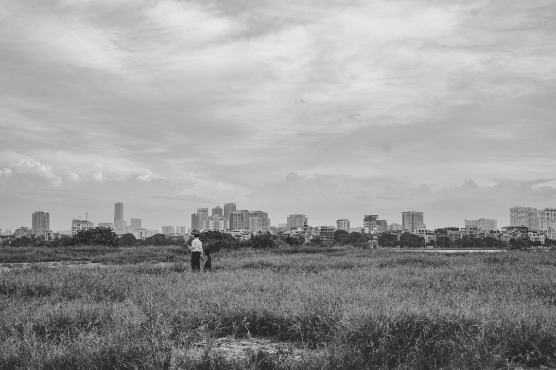 grayscale photo of man in black jacket walking on grass field