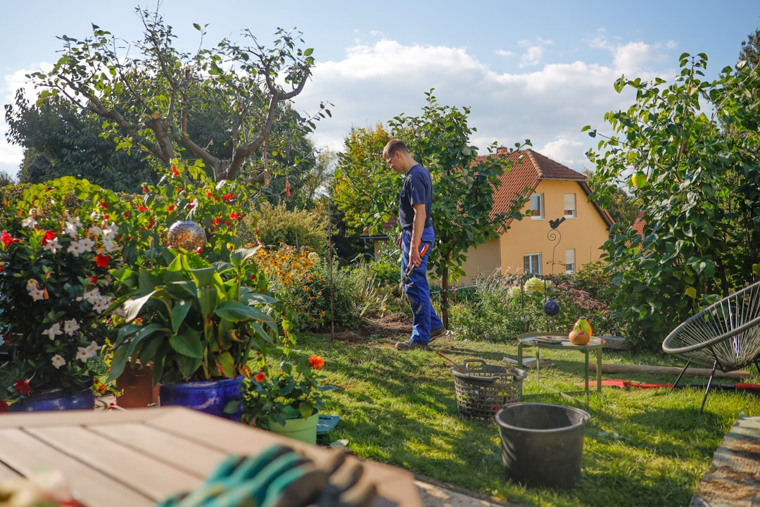Man walks through a lush garden with a house.